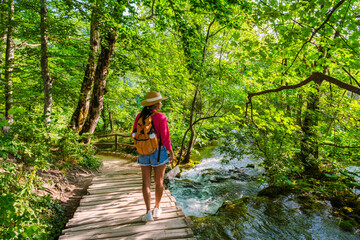 Obraz premium A traveler meanders along a wooden path surrounded by vibrant greenery and cascading waters, immersed in the enchanting beauty of Plitvice Lakes National Park in Croatia during summer