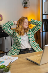 Happy businesswoman sitting at home office desk works on laptop and stretching arms after finishing...