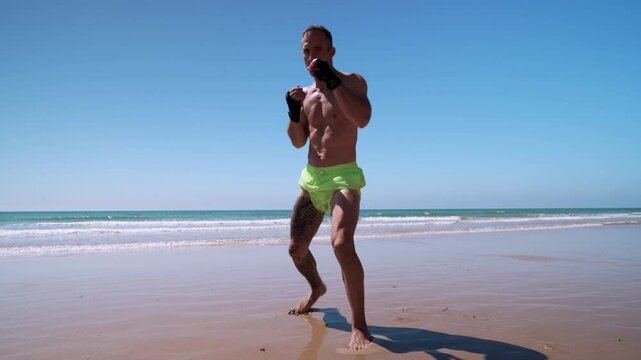 Hombre realizando ejercicios de artes marciales como kick boxing o boxeo en la playa y al fina ataca a la c&aacute;mara con una patada voladora.