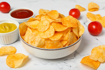 Potato chips in a bowl with sauce and tomatoes on a light background