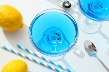 Blue cocktail in glass, whole lemon, straws and ice cubes on white background, top view