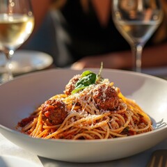 Delicious plate of spaghetti with meatballs garnished with basil and Parmesan cheese, paired with white wine in a cozy dining setting