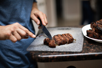 man cutting steak filet mignon into three pieces on a cutting board