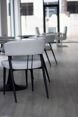 Vertical photo. Empty light interior of canteen, cafe, coworking, cozy office room with white chair, round glass table without people. Desk. City day. Concept of work, job, business, lunch, dinner