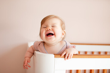 Cute Caucasian baby girl laughing and standing in her crib. Portrait of laughing happy healthy...