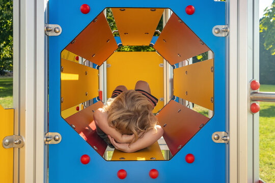 A little boy lies inside a climbing frame on the playground