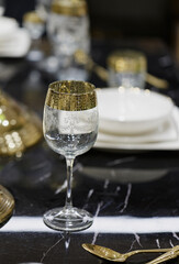 Elegant dining setup featuring crystal glassware and gold accents on a marble table. A beautifully arranged dining table showcases glasses with gold rims, accompanied by white plates and utensils
