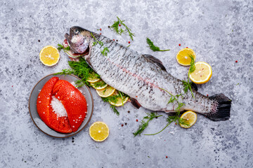Gutted and cleaned raw trout and fresh red caviar with lemon, dill, salt and spices on gray table background, top view