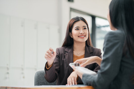 Two women in a business meeting, discussing ideas in a modern office environment, showcasing professional interaction and teamwork.