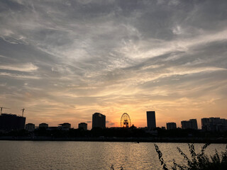 Obraz premium Dramatic Urban Sunset: Silhouetted Ferris Wheel and Skyline Under a Fiery Evening Sky on West Lake in Hanoi, Vietnam