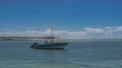 Obraz premium The motorboat is anchored in a calm turquoise ocean. Glare, ripples on the water. Mountains on the horizon. Clouds in the blue sky. Mauritius.
