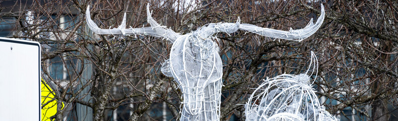 Ornamental reindeer built of white metal frame, white mesh, and white twinkle lights outdoors in a commercial space, celebrating the Christmas holiday season

