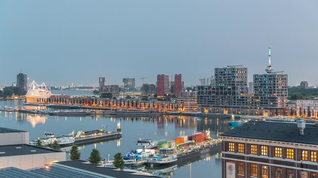 Aerial view over towers in Maashaven night to day transition timelapse with moored ships, Katendrecht and Maas River, Rotterdam before sunrise. Illuminated factory converted to office and event space
