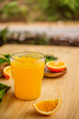 A glass of freshly squeezed orange juice on a wooden table surrounded by orange slices and orange leaves