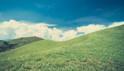 Obraz premium A beautiful countryside landscape with green fields, mountains, and clouds under a blue sky