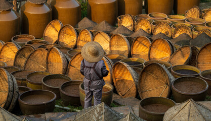 A soy sauce workshop worker works among the many jars in the drying yard.
