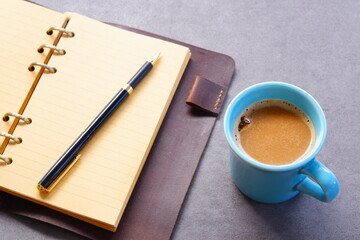 ミルクをたっぷり入れたコーヒー、カフェ・ラッテを飲みながら、システム手帳でデスクワーク中のイメージ
