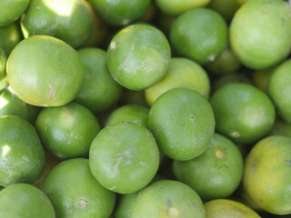 Many fresh limes with green leaves as background, top view