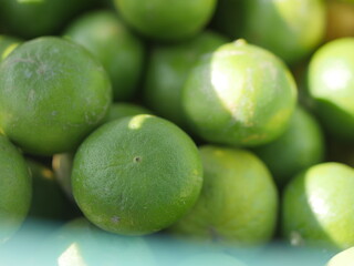 Many fresh limes with green leaves as background, top view