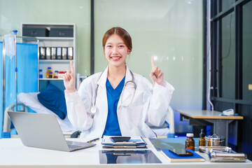A young Asian female doctor, confidently dressed in a white uniform, sits at a computer desk in a...