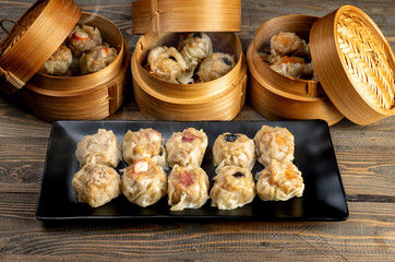 Assorted chinese dim sum dumpling on the plate with bamboo wooden basket bowl on wooden table