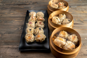 Assorted chinese dim sum dumpling on the plate with bamboo wooden basket bowl on wooden table