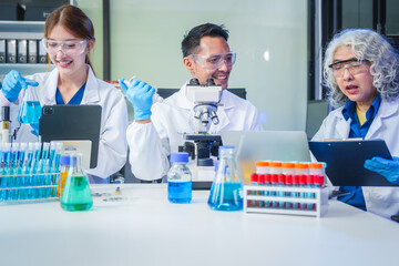 Two Asian men and women sit at a table in a laboratory, conducting research on liquids. They use microscopes, petri dishes, and test tubes filled with various chemicals for analysis