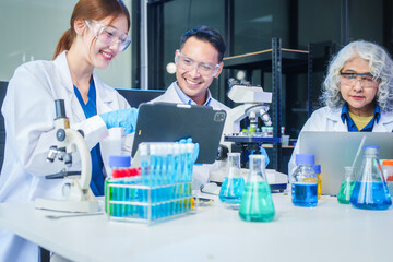 Fototapeta premium Two Asian men and women sit at a table in a laboratory, conducting research on liquids. They use microscopes, petri dishes, and test tubes filled with various chemicals for analysis