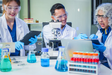 Two Asian men and women sit at a table in a laboratory, conducting research on liquids. They use microscopes, petri dishes, and test tubes filled with various chemicals for analysis