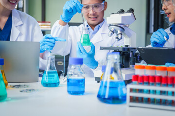 Two Asian men and women sit at a table in a laboratory, conducting research on liquids. They use microscopes, petri dishes, and test tubes filled with various chemicals for analysis