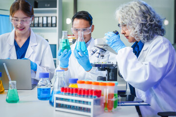 Two Asian men and women sit at a table in a laboratory, conducting research on liquids. They use microscopes, petri dishes, and test tubes filled with various chemicals for analysis