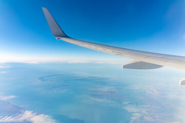 View from the airplane window at a beautiful blue clear sky, earth, sea and the airplane wing