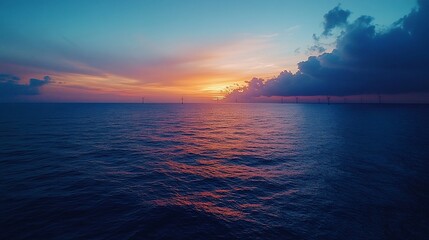Vibrant sunset over calm ocean with offshore wind turbines.