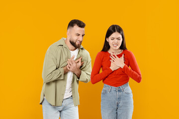 Obraz premium A young European couple stands close together, both placing their hands over their chests, conveying deep feelings of love and affection. Their expressions reflect a strong emotional connection.