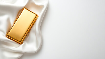 Gold bar on a white satin textile background, ingot and money elegance concept image with copy space