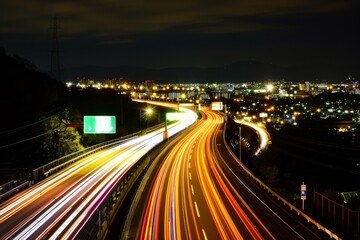 The highway is illuminated by streaks of light from moving vehicles, with a bustling city skyline in the background under a dark night sky.