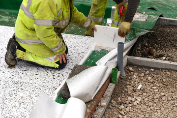 Construction workers installing waterproofing membrane and insulation  on a building foundation in a green field