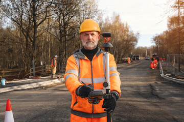 Site engineer surveys road project in autumn landscape with safety gear and accurate equipment