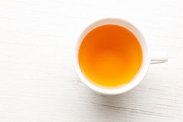 Cup of hot tea blended from rooibos, spearmint, apple, baobab on white wooden table.