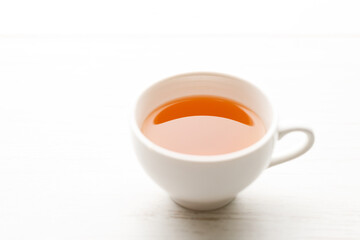 Cup of hot tea blended from rooibos, spearmint, apple, baobab on white wooden table.