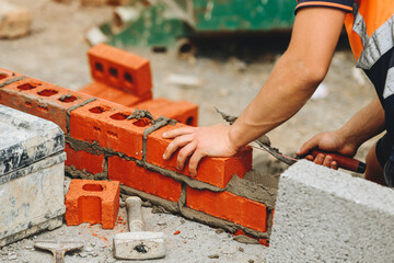 Bricklayer constructs a wall with red bricks at a construction site during the day