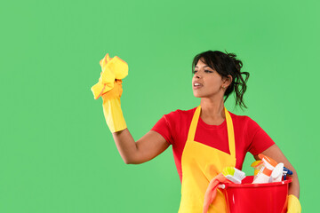 Woman cleaning with enthusiasm while holding a bucket of cleaning supplies against a green background