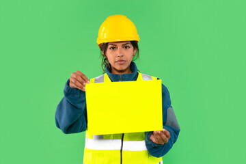 Young construction worker holds bright yellow sign against green background during safety training session