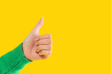 Hand giving a thumbs up gesture against a bright yellow background conveying positivity and approval