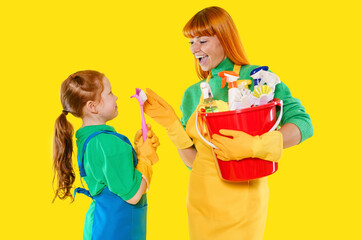 Mother and daughter enjoy cleaning together with colorful supplies on a bright yellow backdrop