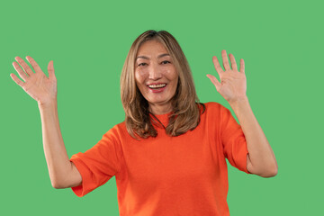 Smiling woman wearing an orange shirt waves her hands enthusiastically against a green background
