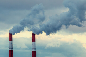 Thick clouds of gray smoke billow from tall industrial smokestacks against a backdrop of overcast...