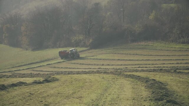 A tractor with hay baler or hay maker trailer in the green field