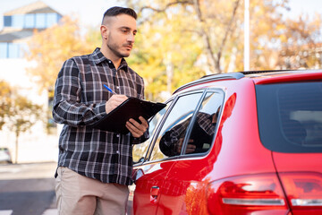 Fototapeta premium Insurance agent writing information on clipboard near red car during insurance claim process on a city street