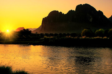 Sunset over Nam Song River with silhouetted rock formations in Vang Vieng, Laos